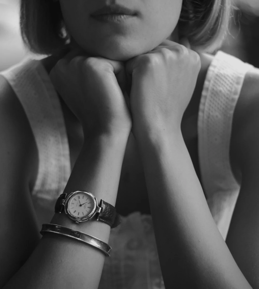 A woman resting her chin on her hands, wristwatch and bangle visible, in black and white